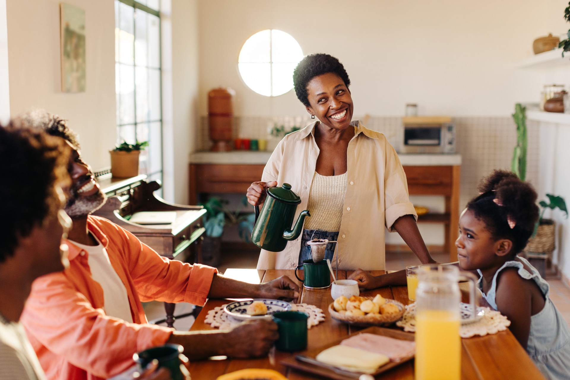 Family breakfast in a Brazilian home: Happy black family sharing a delicious morning meal with drip coffee and pão de queijo